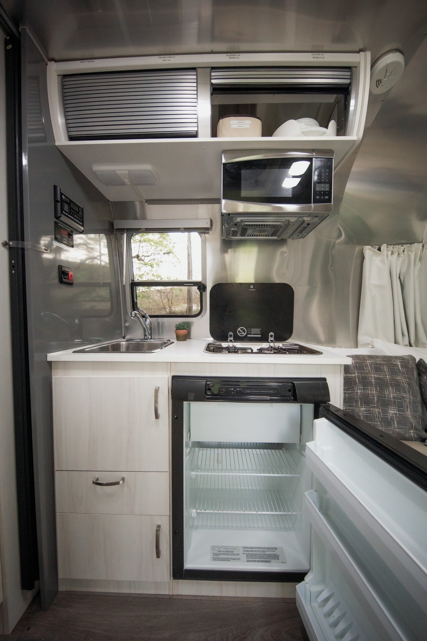 This rv rental's compact kitchen features a sink, stove, microwave, and open fridge with labeled overhead storage.