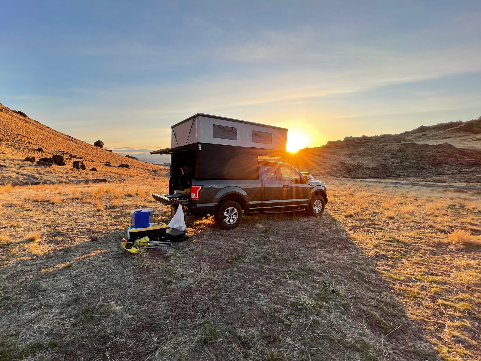Truck camper RV rental set up for a golden hour outdoor adventure at sunset in a vast, dry landscape.