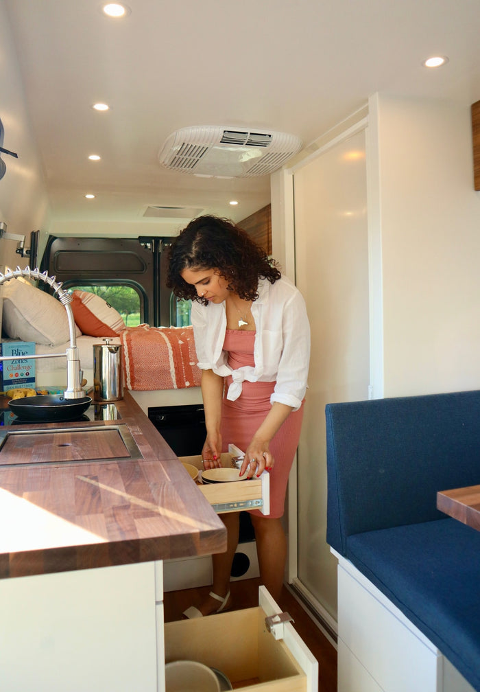 ready for your RV rental journey. Parked by a dark wall.|Inside an RV rental van: custom storage below a raised bed