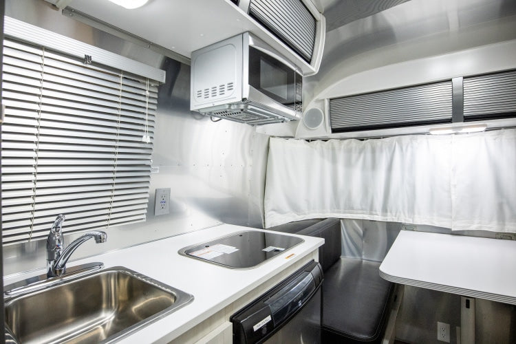 RV rental interior: A compact kitchen with sink, cooktop, microwave, and dining area, ideal for travel.