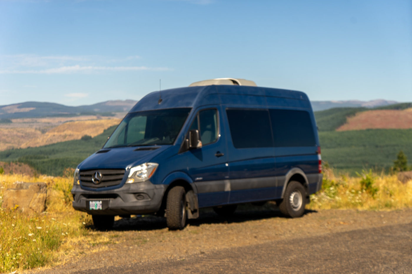 and front seats.|Dark Mercedes Sprinter rv rental parked among tall trees on a sunny day.|Experience comfortable **rv rental** travel in this spacious camper van — photo 4