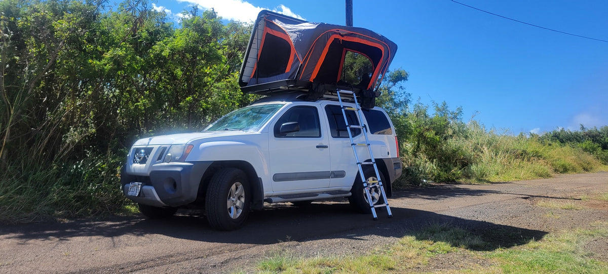 White Nissan Xterra SUV with a deployed rooftop tent and ladder. This RV rental is ready for outdoor adventure.