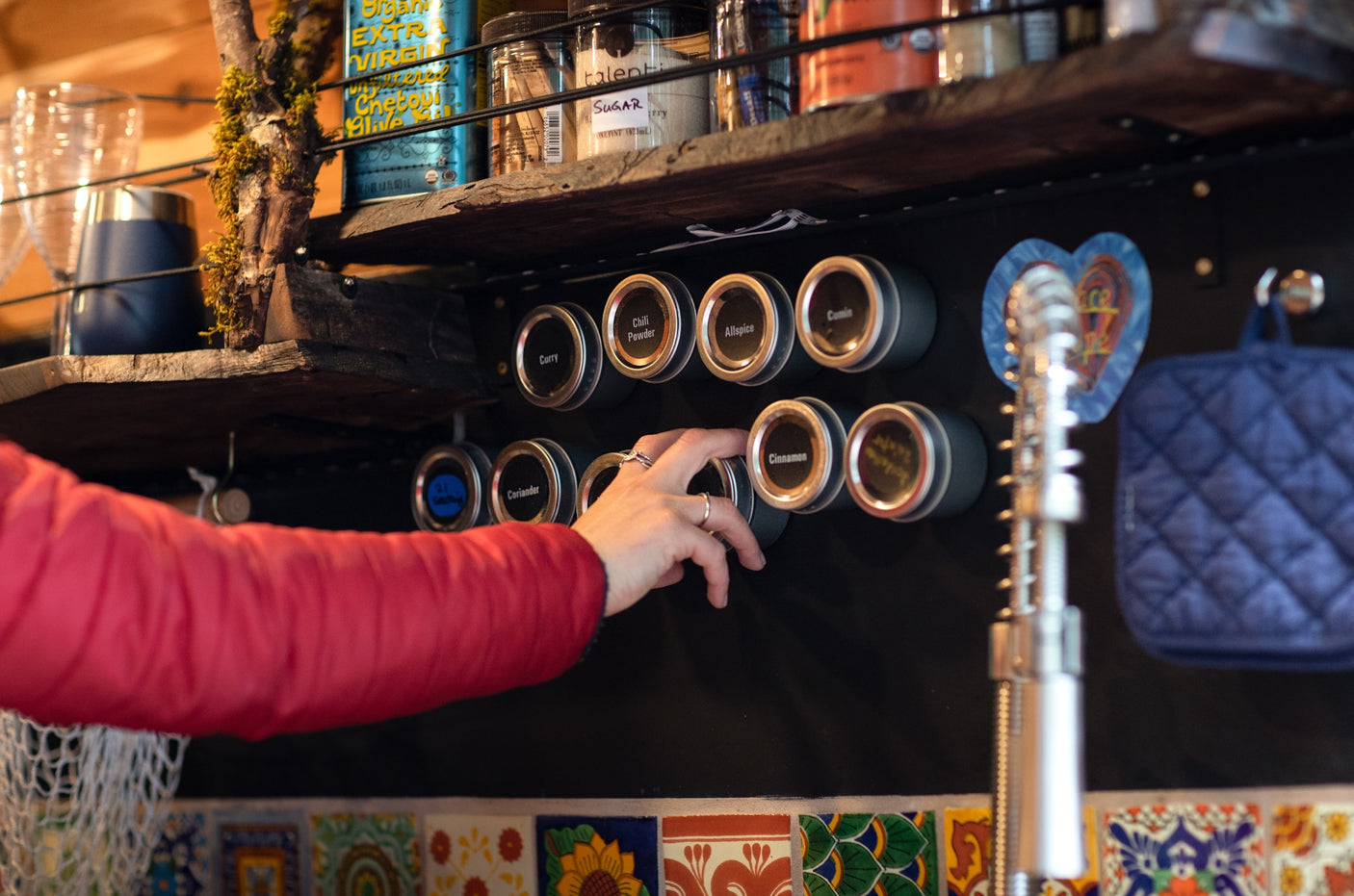 Person's hand reaches for a spice jar on a magnetic rack, showcasing compact kitchen organization in an RV rental. Cooking essentials.