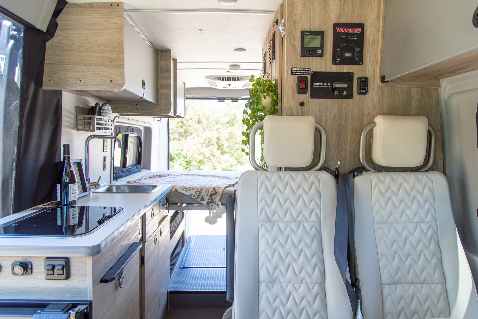 Bright rv rental interior: compact kitchen, comfortable rear bed, front seating, and essential control panels.