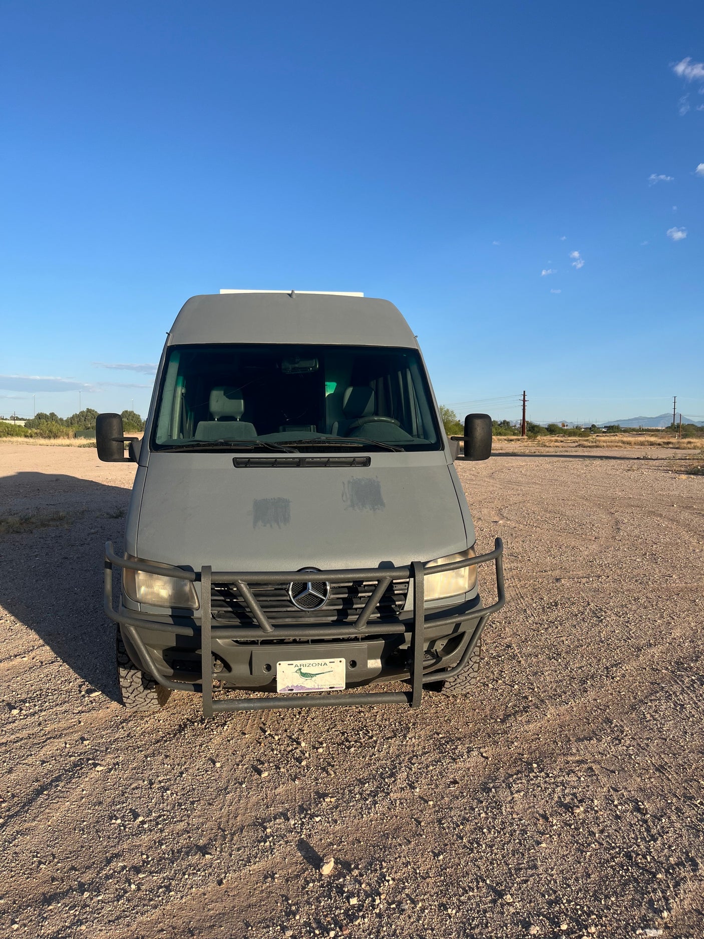 Gray Mercedes-Benz Sprinter van with bull bar, ideal for rv rental adventures. Parked on gravel under a clear Arizona sky.