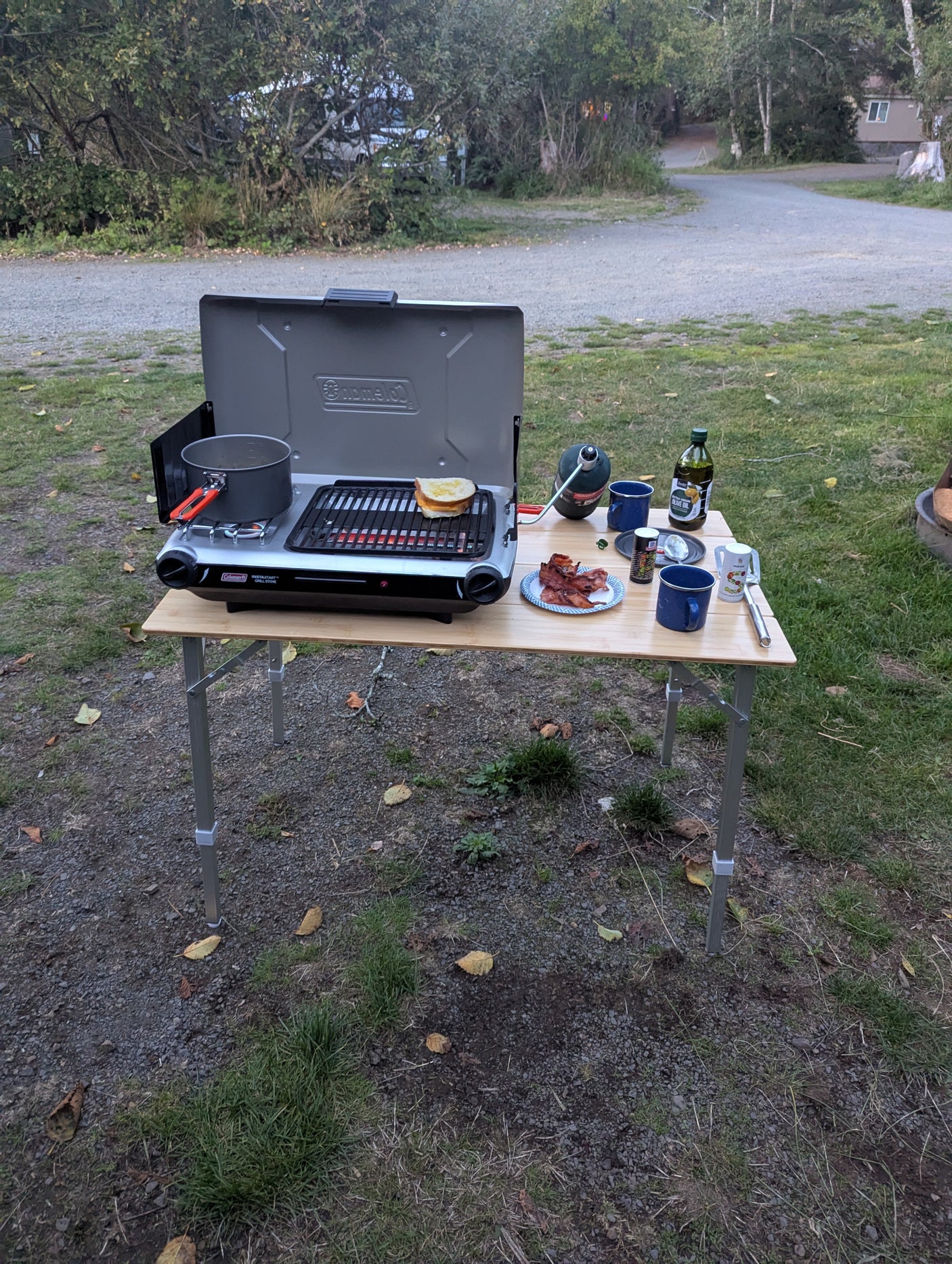 Outdoor camping breakfast: grilled cheese, bacon, and a pot cooking on a Coleman portable stove. Perfect for an RV rental trip!