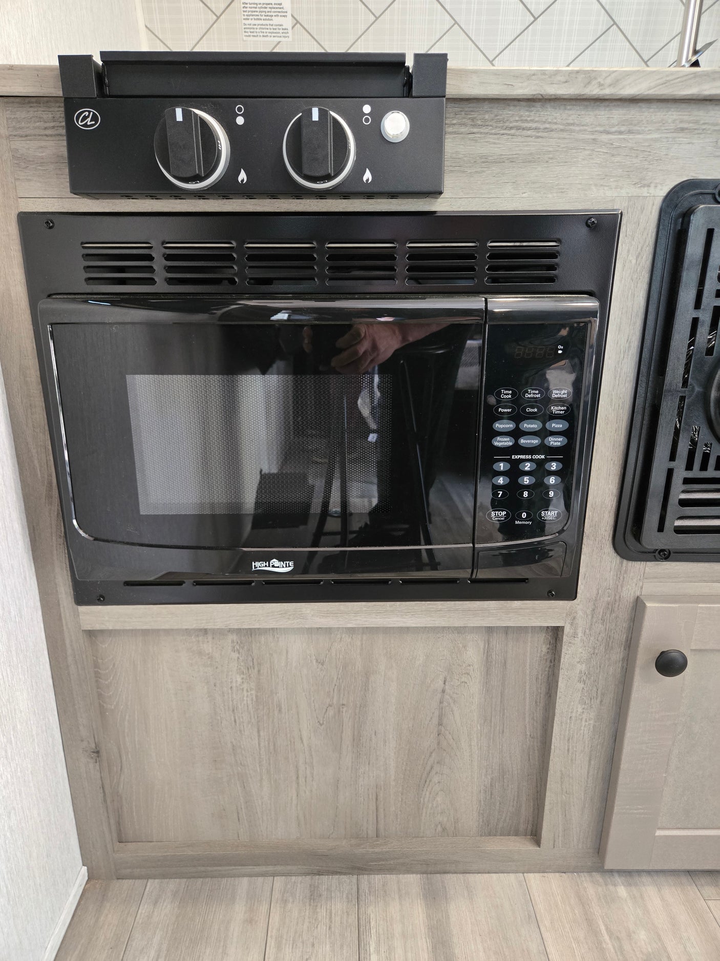 An rv rental kitchen with a built-in High Pointe microwave and two-burner cooktop, integrated into light wood cabinetry.