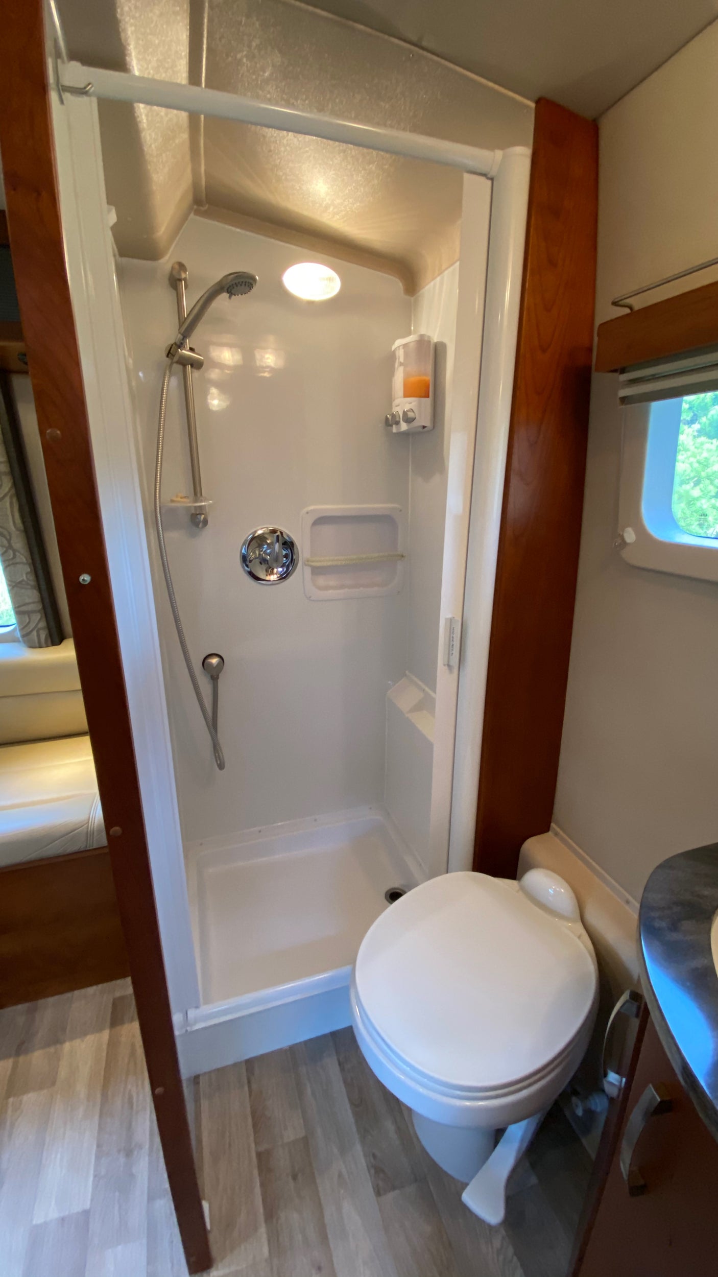 RV rental bathroom features a compact white shower stall with handheld shower, soap dispenser, and toilet.