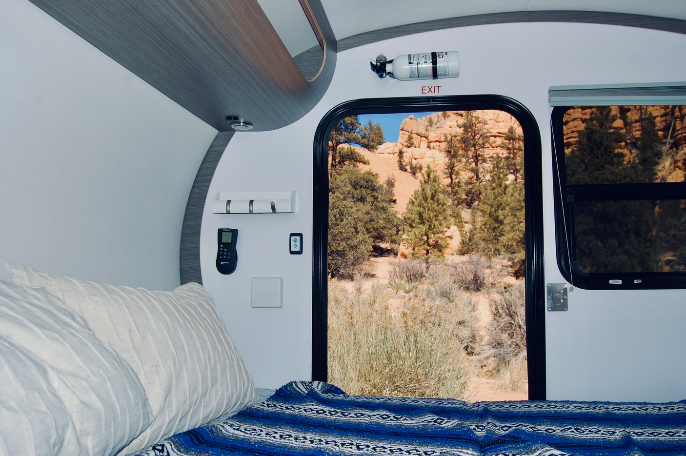 Experience a comfortable RV rental. Inside, a bed, fire extinguisher, and controls. Outside, a stunning desert landscape through the open door.