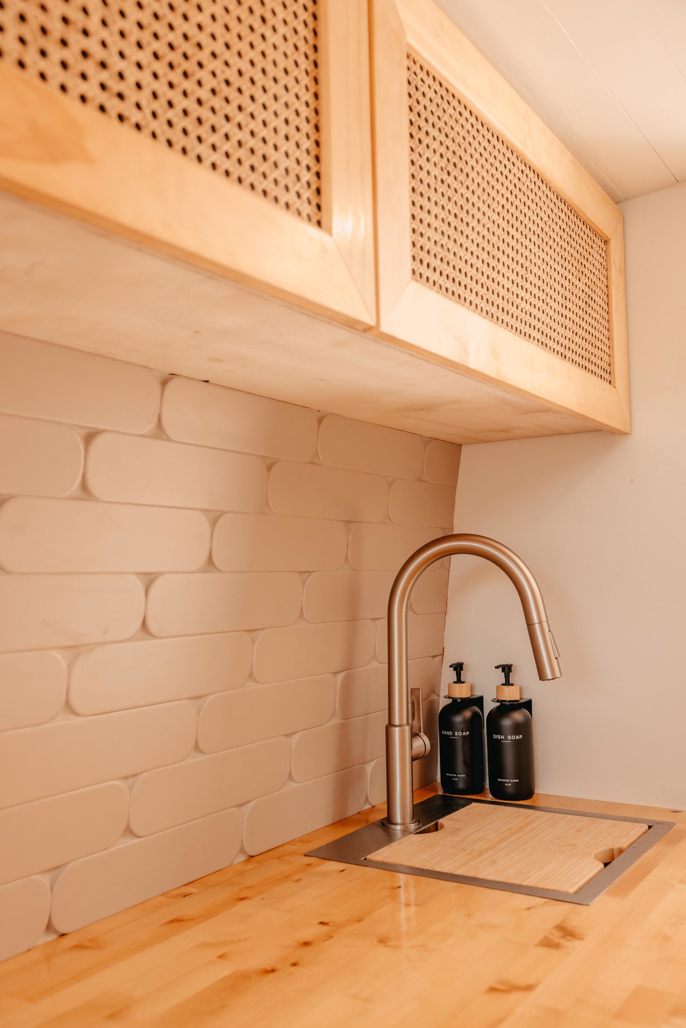 Modern RV rental kitchen with natural wood cane cabinets, unique beige tiles, and sleek stainless steel faucet.