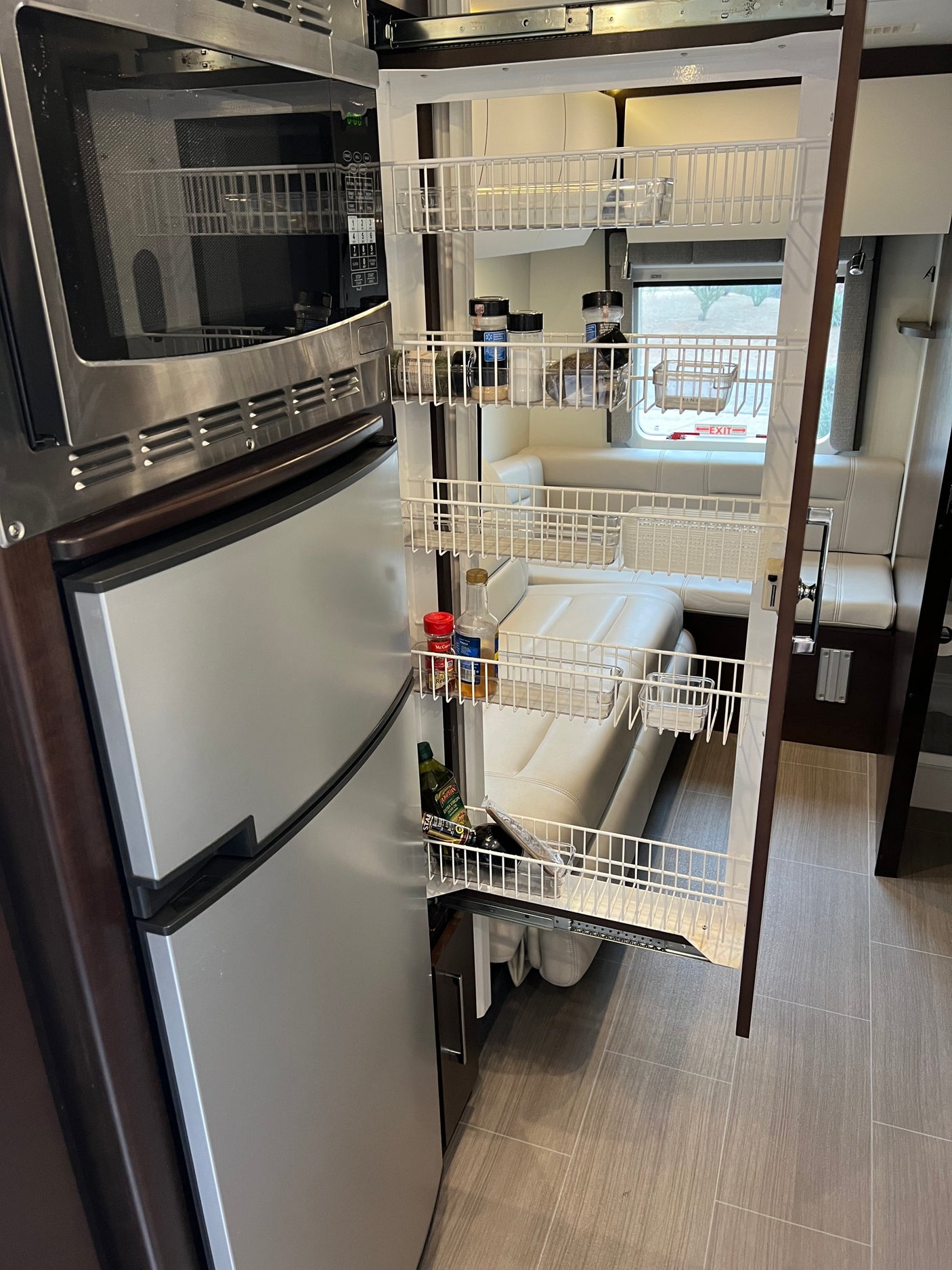 An RV rental interior featuring a stainless steel refrigerator, microwave, and a full pull-out pantry organizing kitchen essentials.