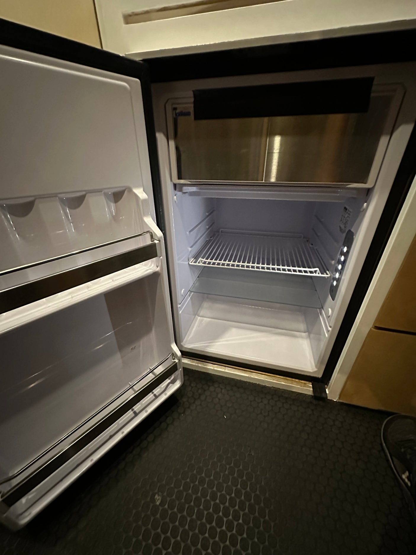 Clean, empty RV rental refrigerator with a freezer, wire shelves, and bright LED lighting, ready for your adventure.