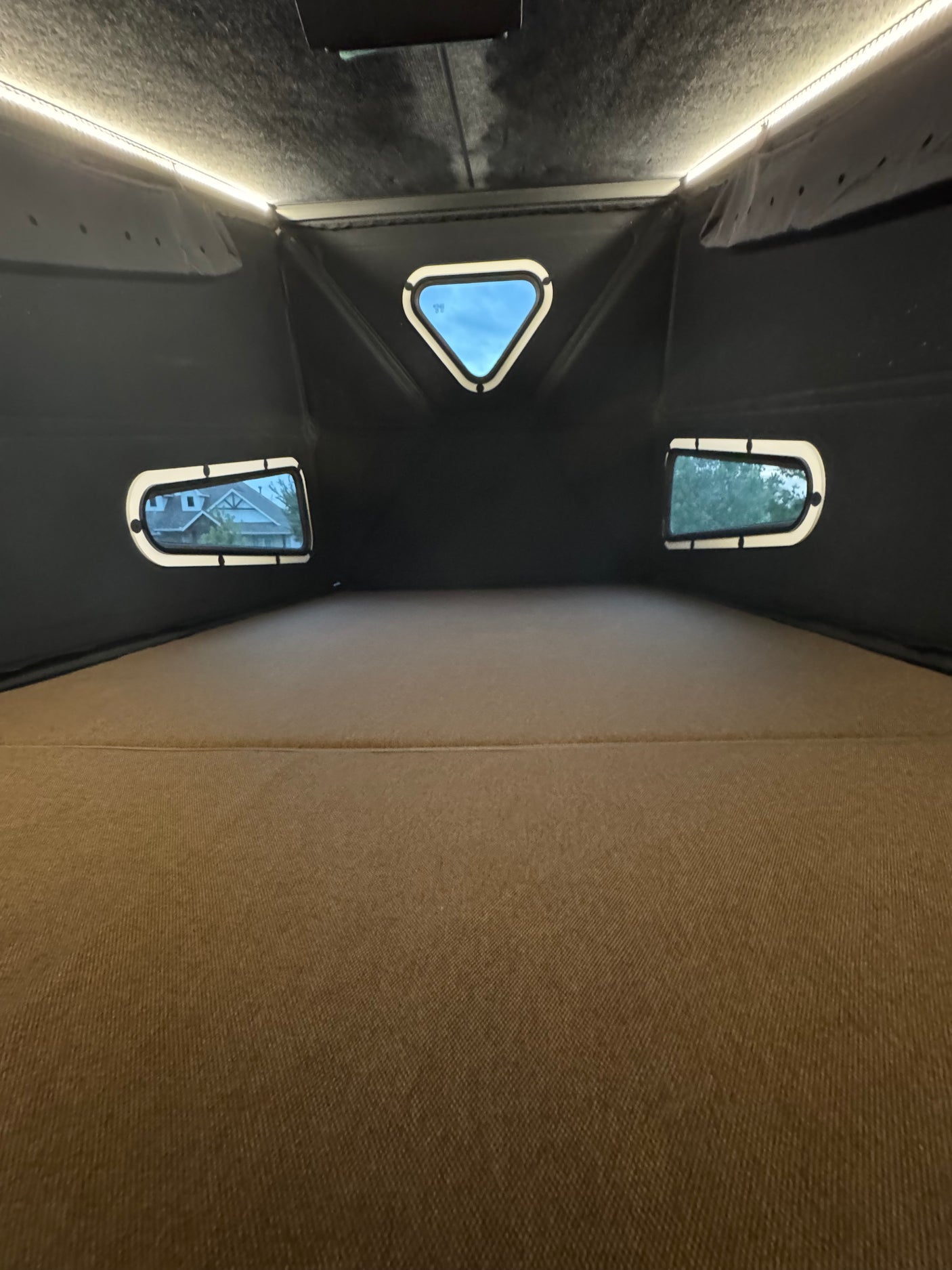 Cozy RV rental interior: spacious sleeping area with overhead lighting & windows offering outdoor views in a pop-top camper.