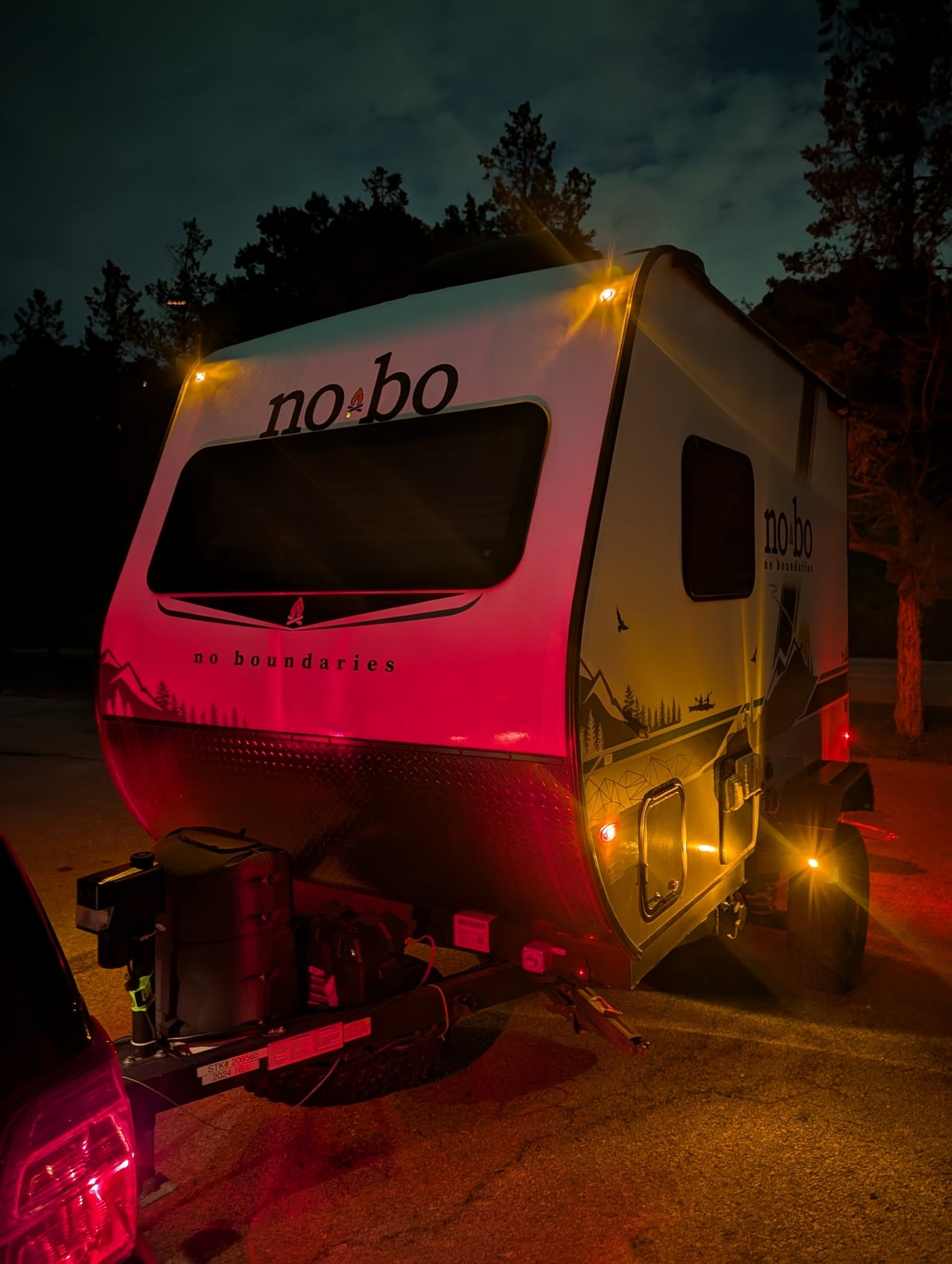 Nighttime rv rental featuring a No Boundaries travel trailer hitched to a car, illuminated by vibrant red and amber lights.