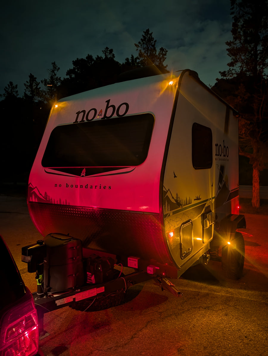 Nighttime rv rental featuring a No Boundaries travel trailer hitched to a car, illuminated by vibrant red and amber lights.