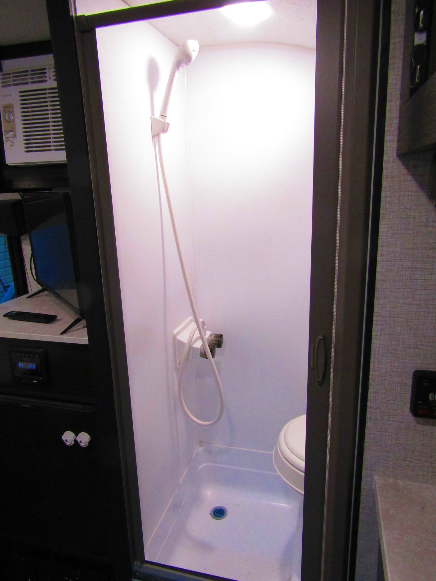 RV rental: View of a compact wet bath featuring a shower, toilet, and nearby air conditioner and entertainment unit.