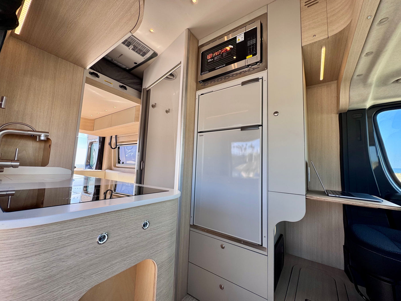 Modern RV rental interior: kitchenette with fridge/microwave, sleek design, and compact workspace for mobile living.