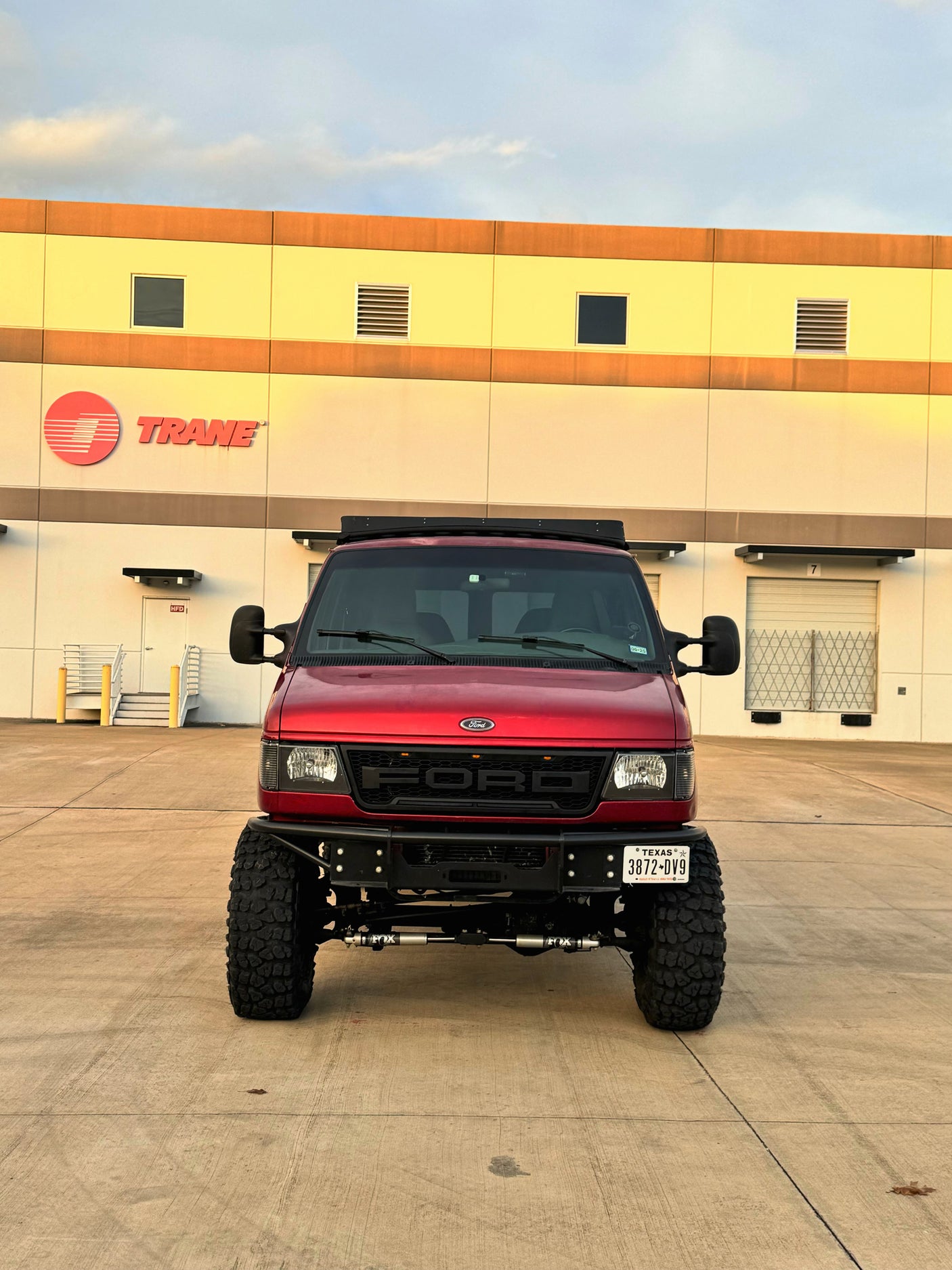 Custom red Ford adventure van, ideal for an rv rental, parked at a Trane facility in Texas.