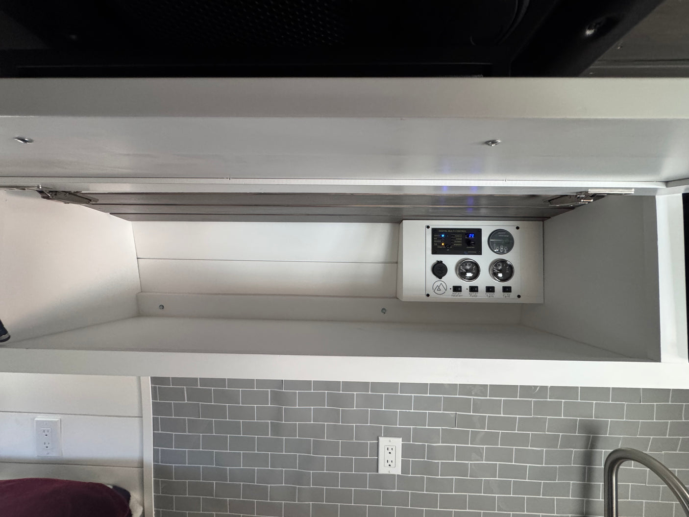 RV rental control panel: digital display, water heater, pump, fresh & gray tank gauges in overhead cabinet.
