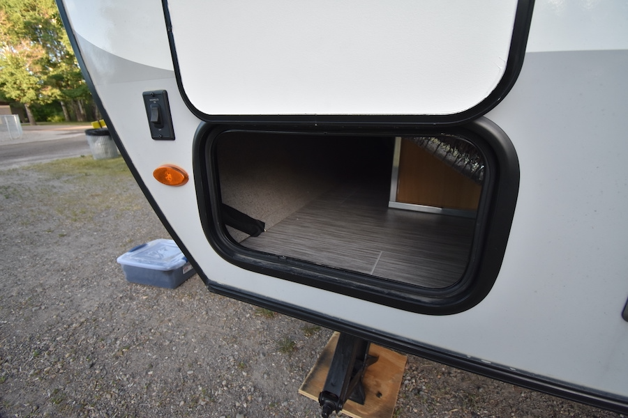 Open storage on an RV rental, showing a large exterior compartment with light interior flooring. An orange marker light & switch are visible.