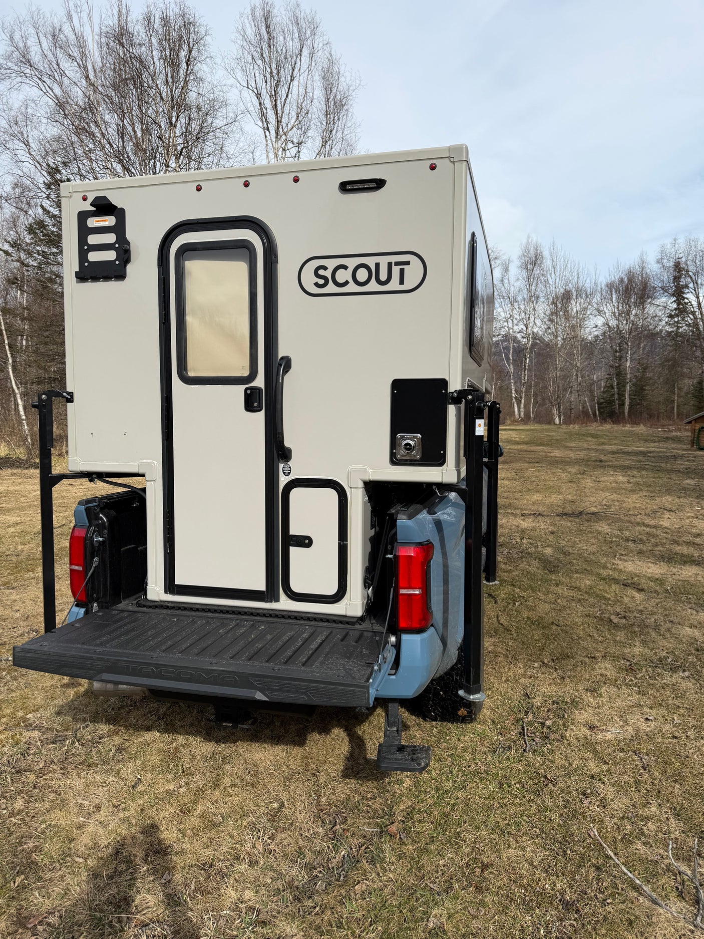Rear of a Scout truck camper mounted on a blue pickup truck in a grassy field. Consider this RV rental for your next adventure.