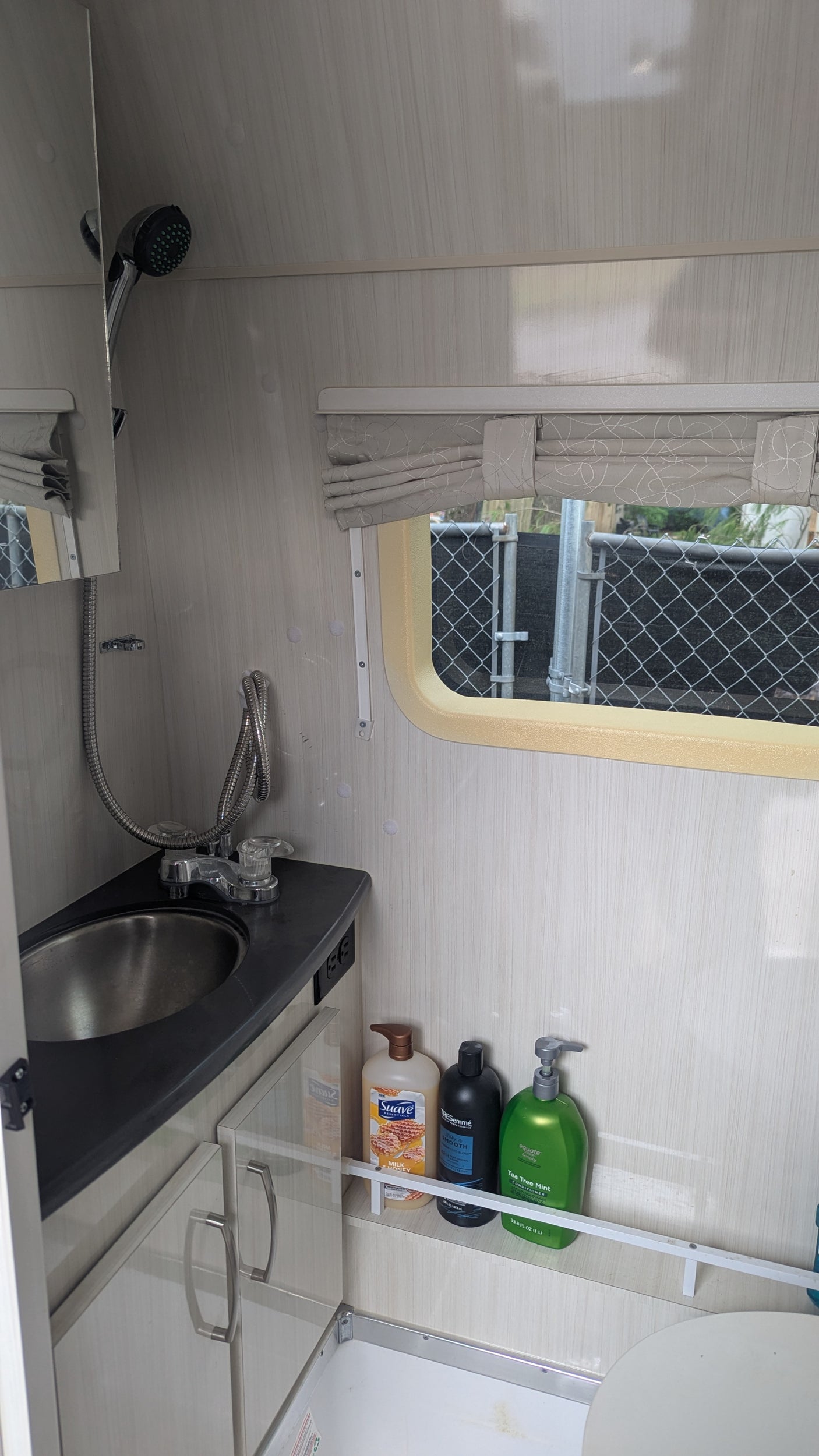 This compact rv rental bathroom features a sink, extendable shower, window, and toiletries on a shelf. Ready for your next adventure.