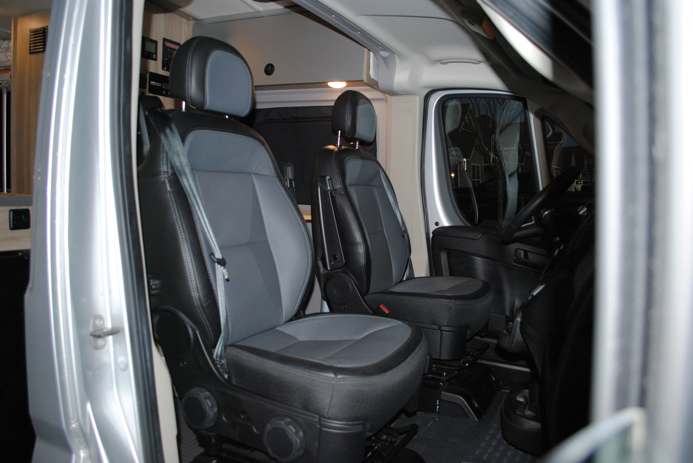 RV rental's spacious front cabin with comfy black & gray driver and passenger seats, ready for adventure.