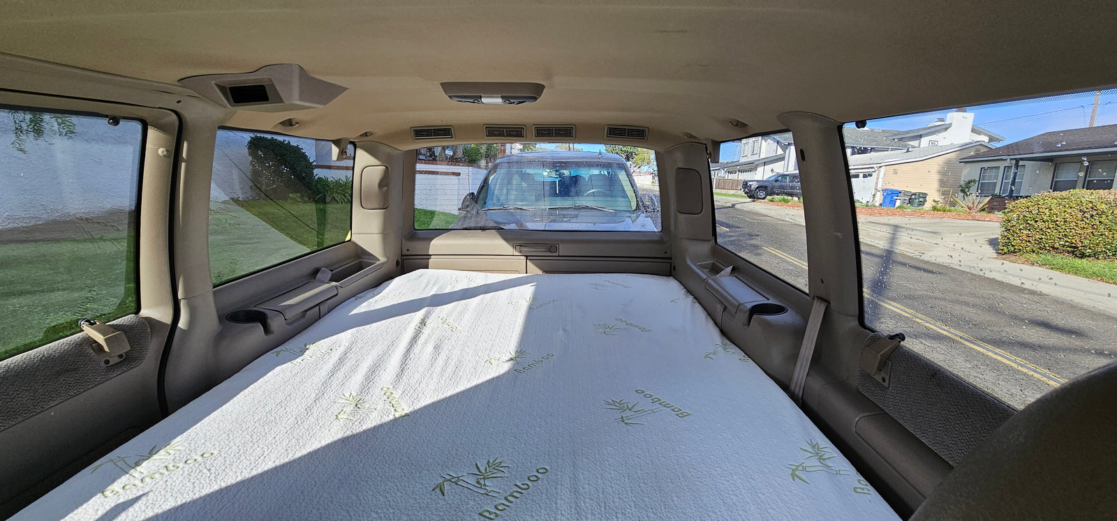 Interior of an RV rental showing a bamboo mattress set up for sleeping, with a view of a residential street outside.