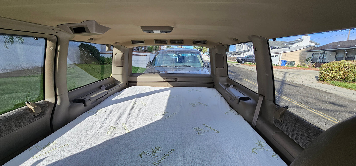Interior of an RV rental showing a bamboo mattress set up for sleeping, with a view of a residential street outside.