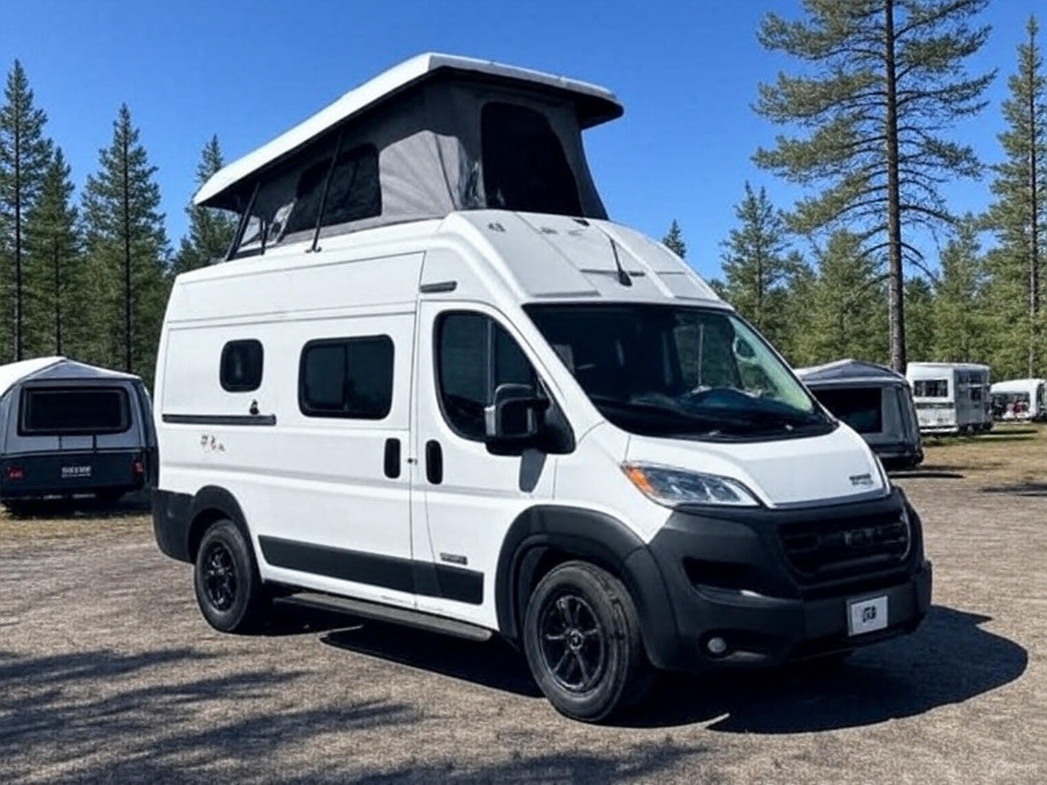 White pop-top camper van parked outdoors among trees