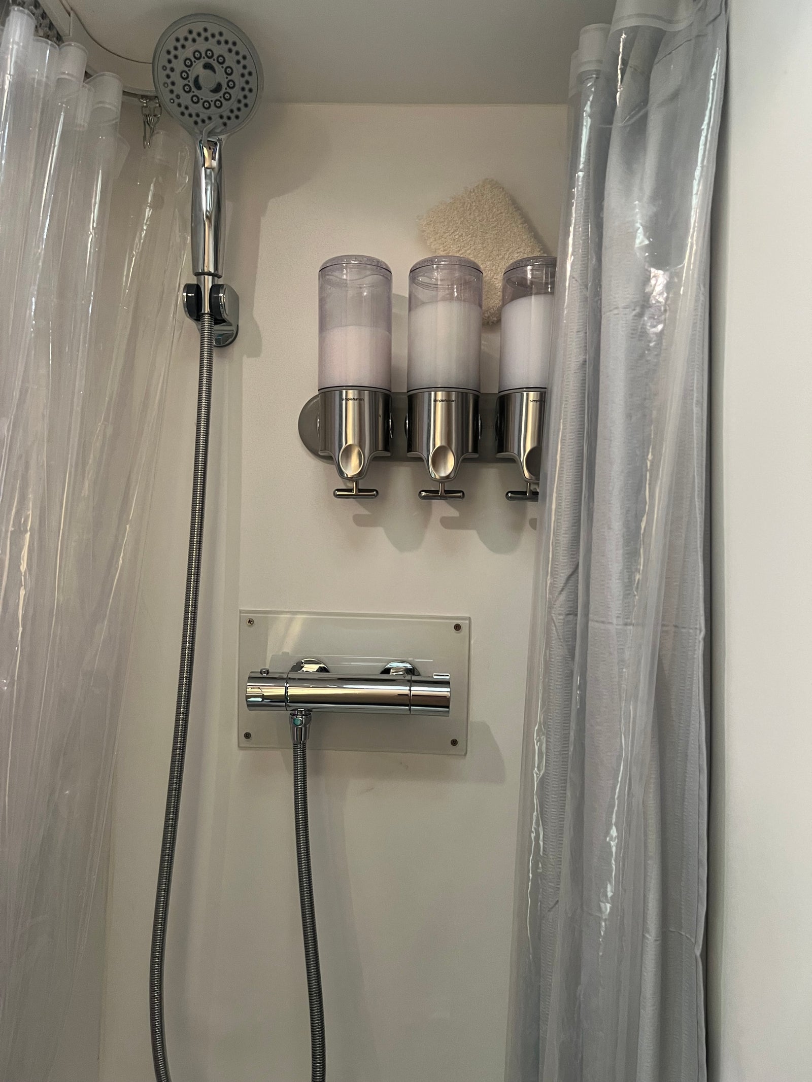 Inside an RV rental: a modern shower with a handheld head, triple wall-mounted dispensers, controls, and dual curtains.