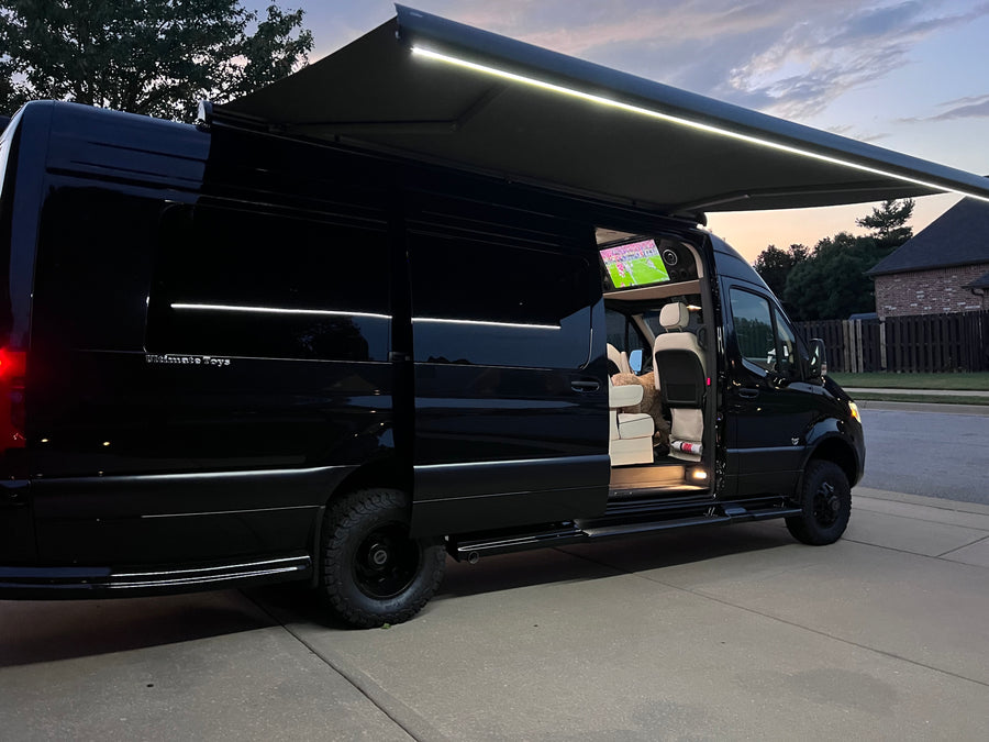 Luxury black Sprinter van with lit awning and interior TV showing sports; an excellent rv rental option.|A black Sprinter van