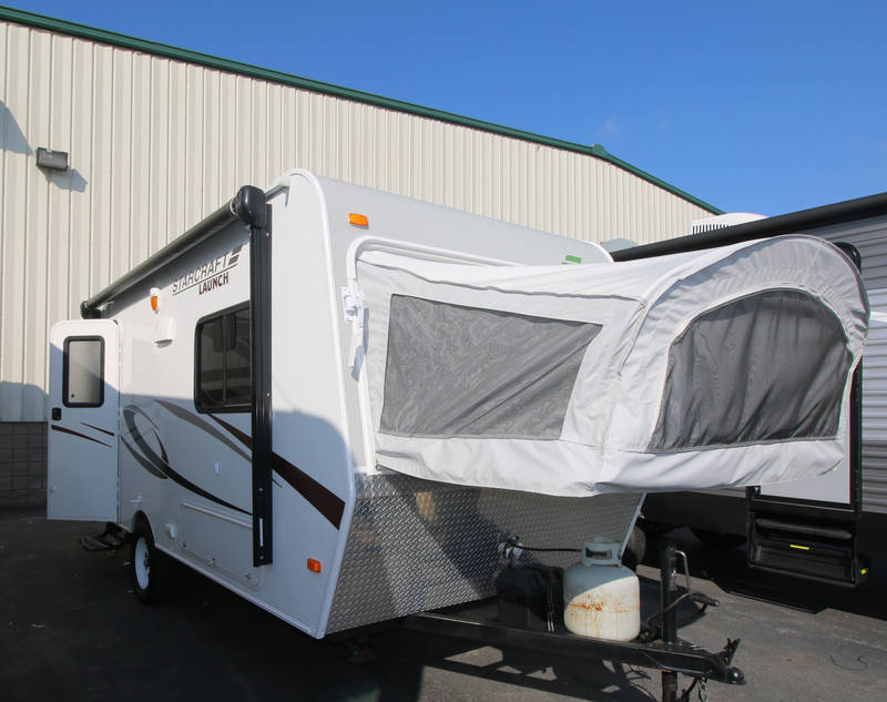 Discover this Starcraft Launch hybrid RV rental with its front canvas pop-out bed extended. The side door is open, and a propane tank is visible, ready for your trip.