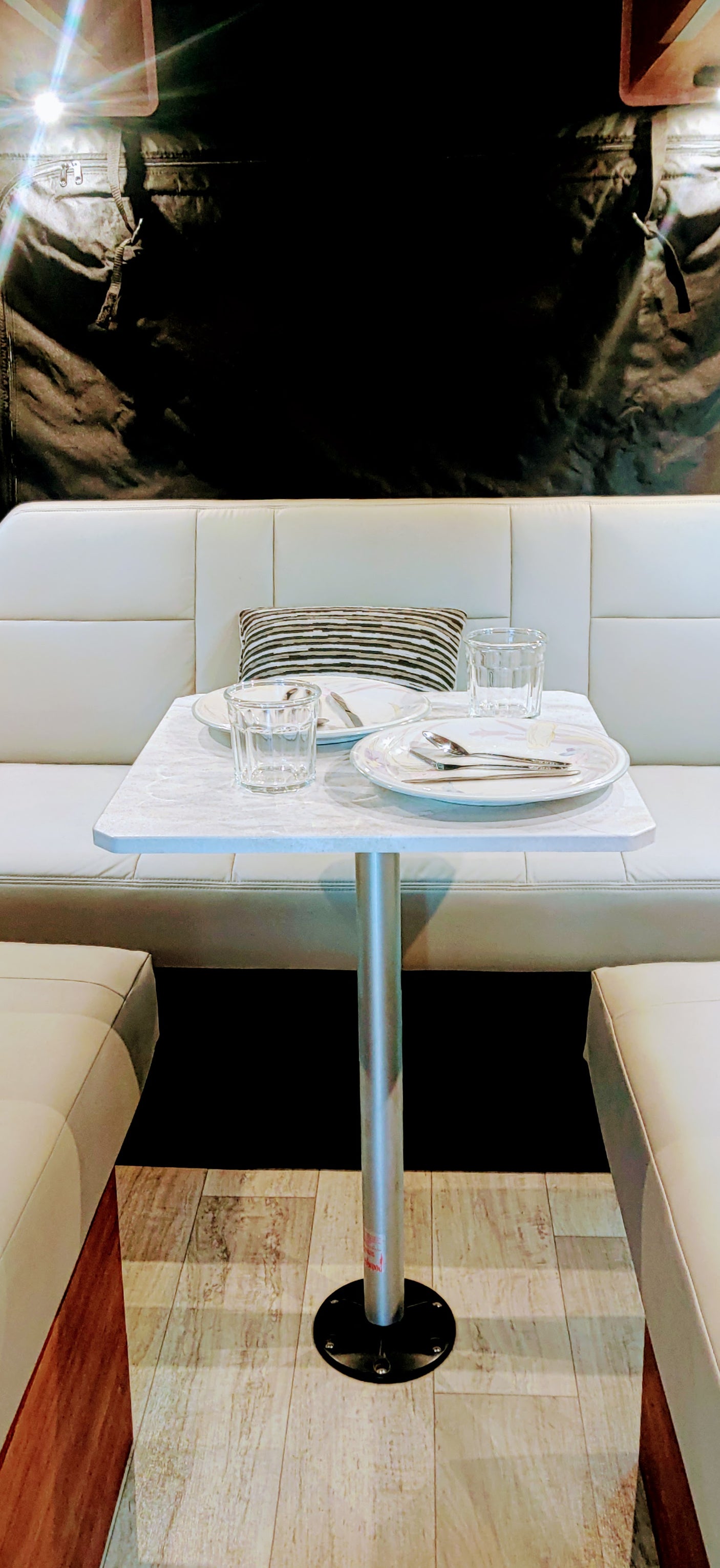 RV rental dinette: Clean white benches, set table with glasses & plates, ready for meals in a modern interior.