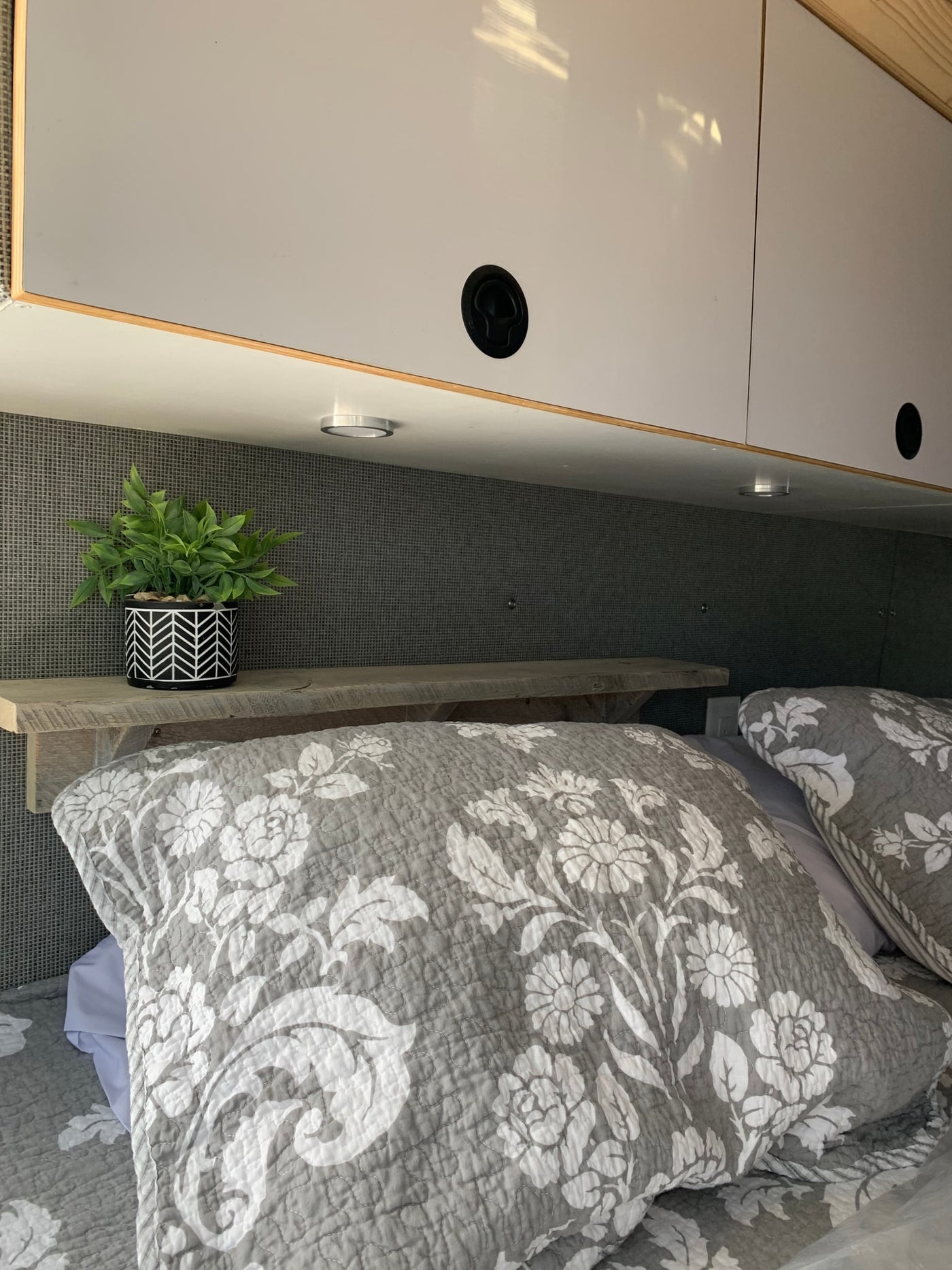 Cozy RV rental bedroom showcasing smart overhead storage, a small plant on a wood shelf, and soft floral bedding. — photo 3