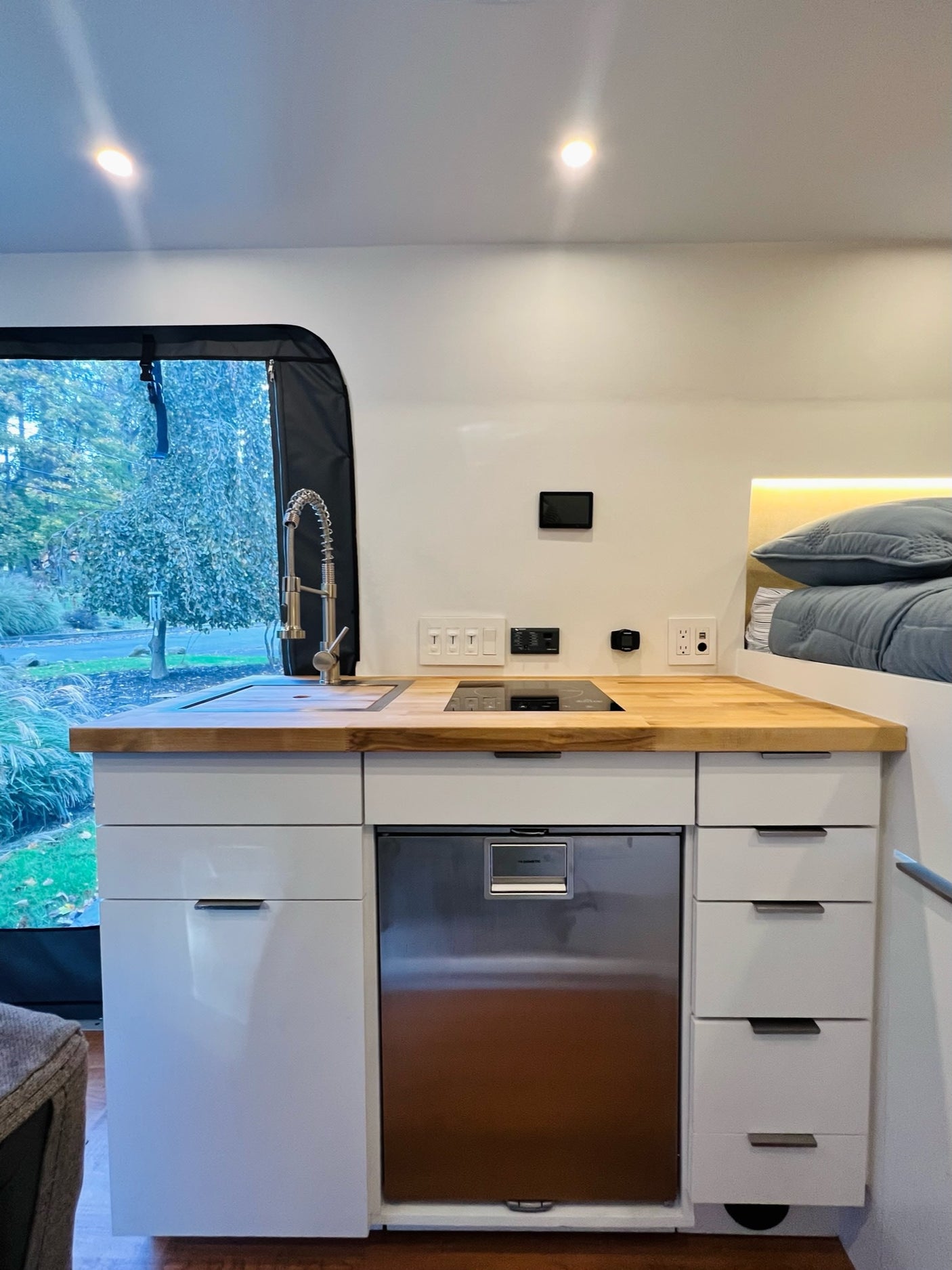 Explore this modern rv rental's interior! Features a compact kitchen with wood counter, integrated fridge, and cozy bed.
