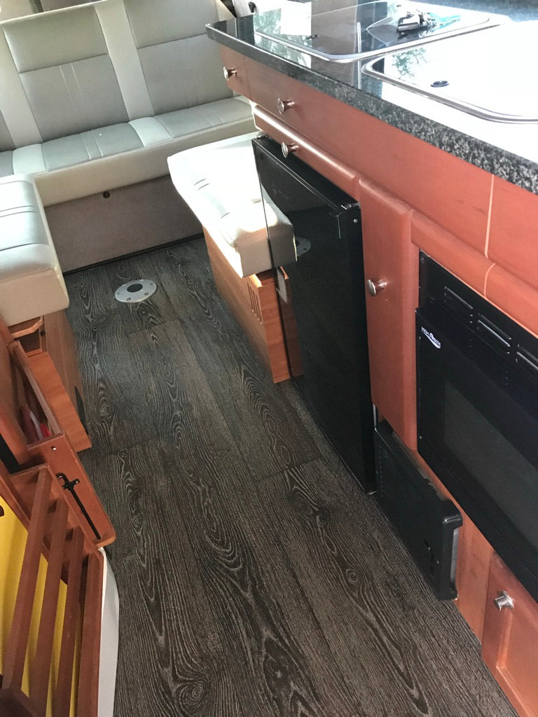 Compact rv rental interior with dark wood flooring, light seats, and a kitchenette featuring a sink, fridge, and microwave.