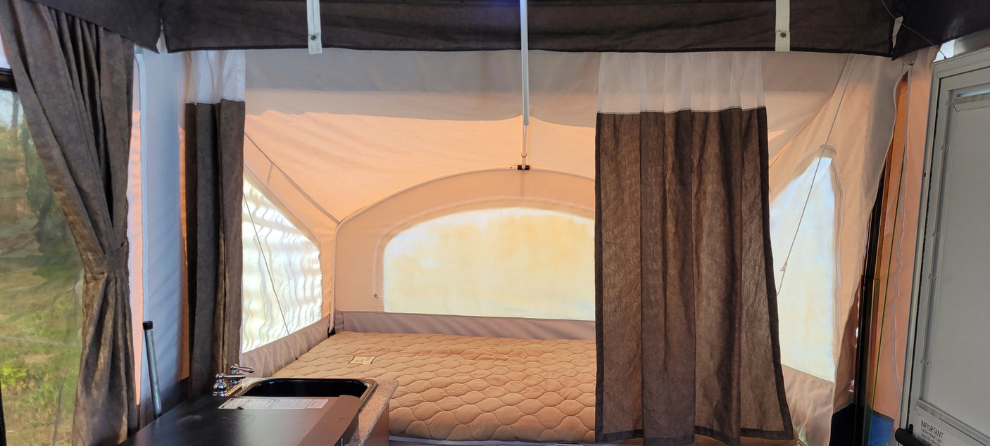 Cozy interior of an RV rental pop-up camper, showing a bed, brown curtains, and a small sink area.