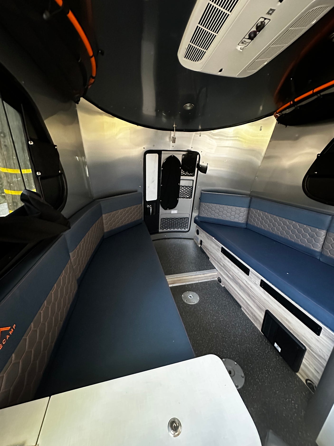 View inside a modern rv rental camper featuring blue convertible bench seats, a removable table, and sleek aluminum walls.