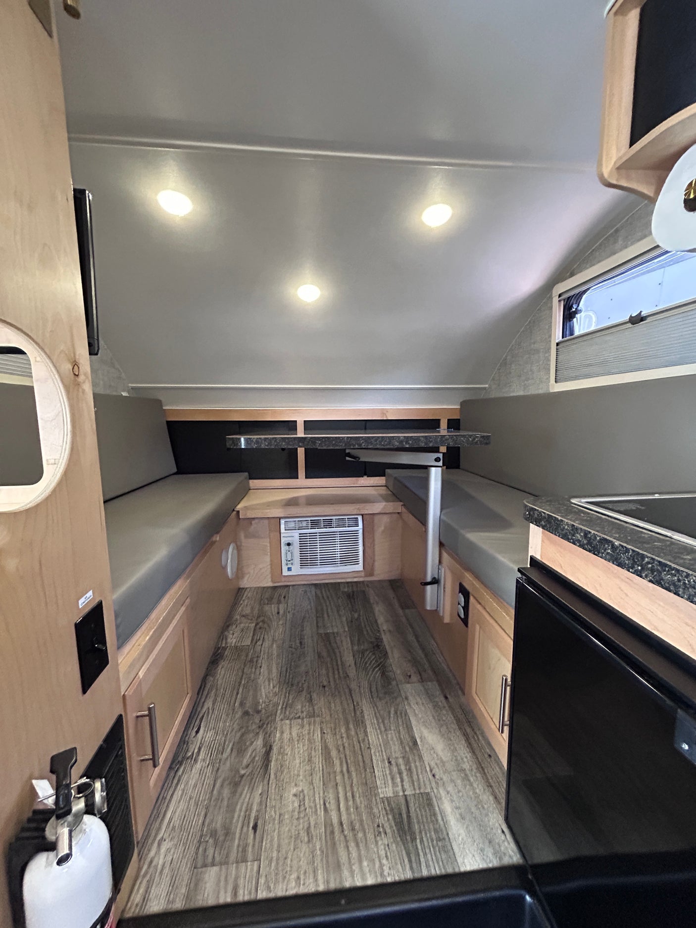 This compact RV rental or camper interior showcases a dining booth, kitchenette, AC unit, and overhead lighting.
