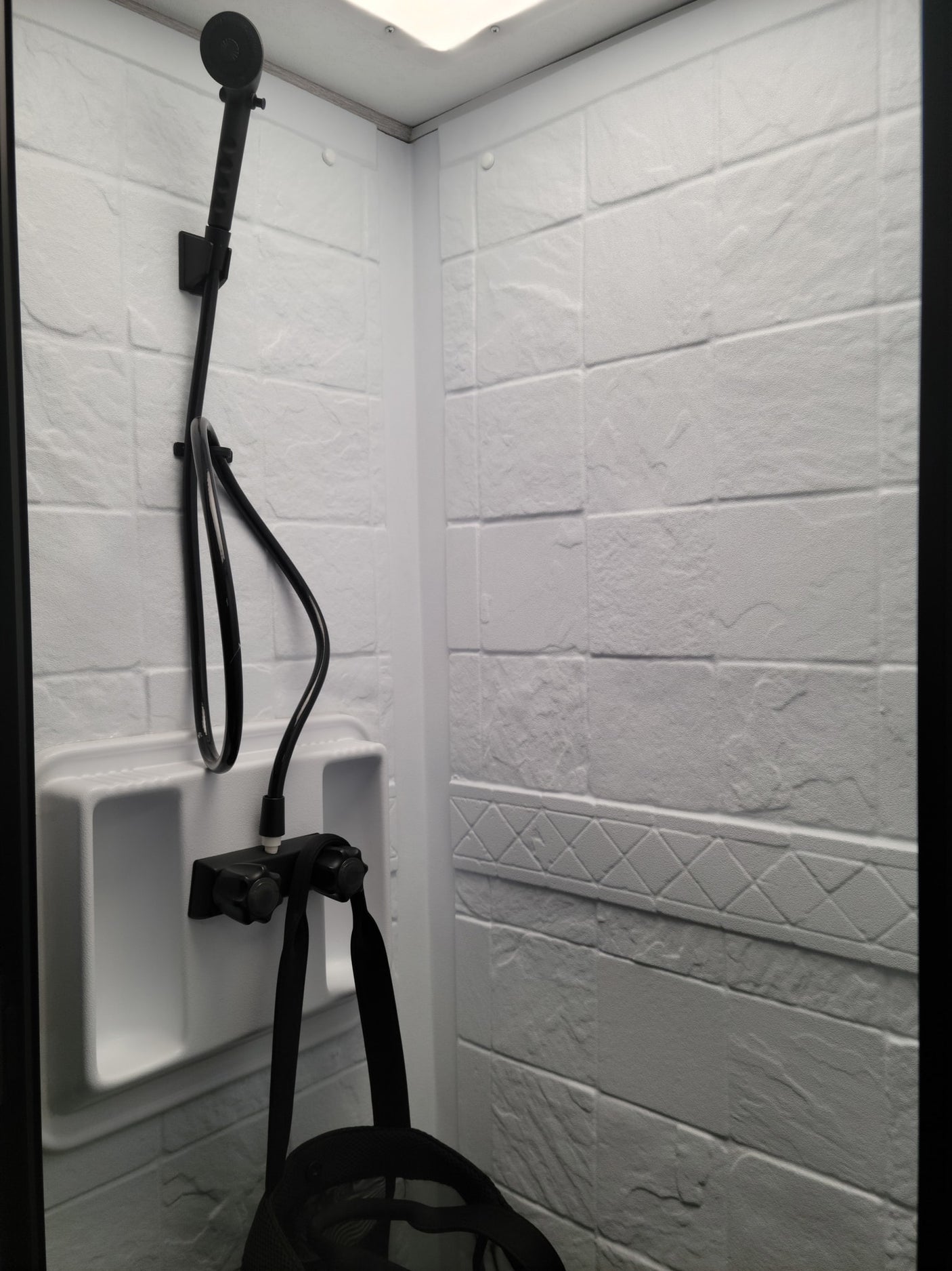 Compact RV rental shower: white textured walls, black handheld showerhead, and controls. Clean, functional bathroom for travel.