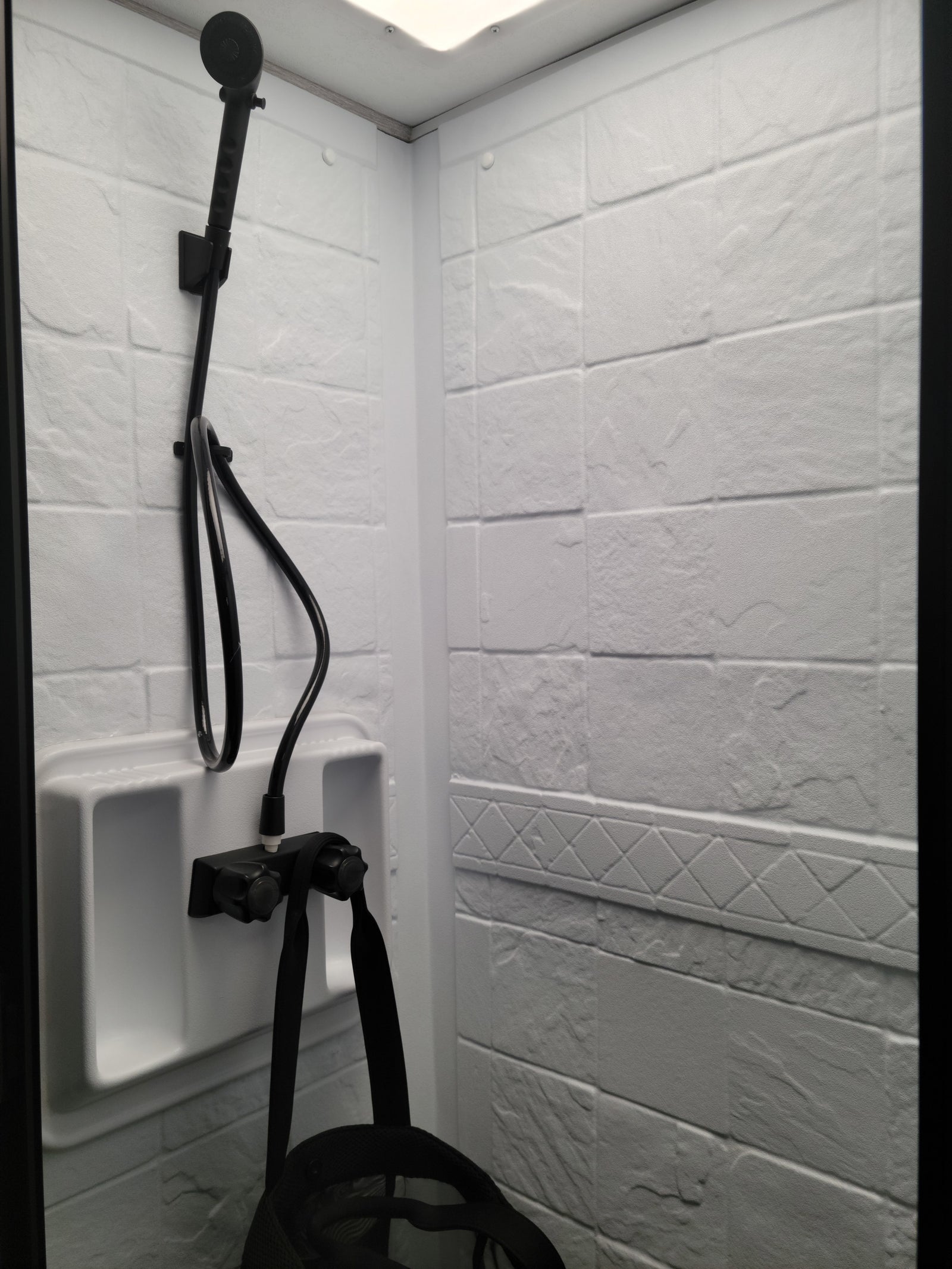 Compact RV rental shower: white textured walls, black handheld showerhead, and controls. Clean, functional bathroom for travel.