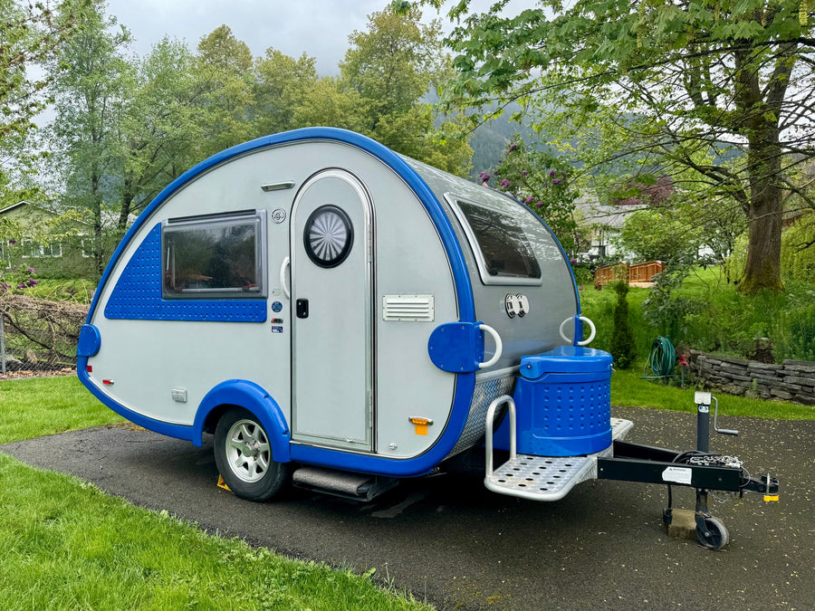 A blue & grey teardrop RV rental camper parked on asphalt