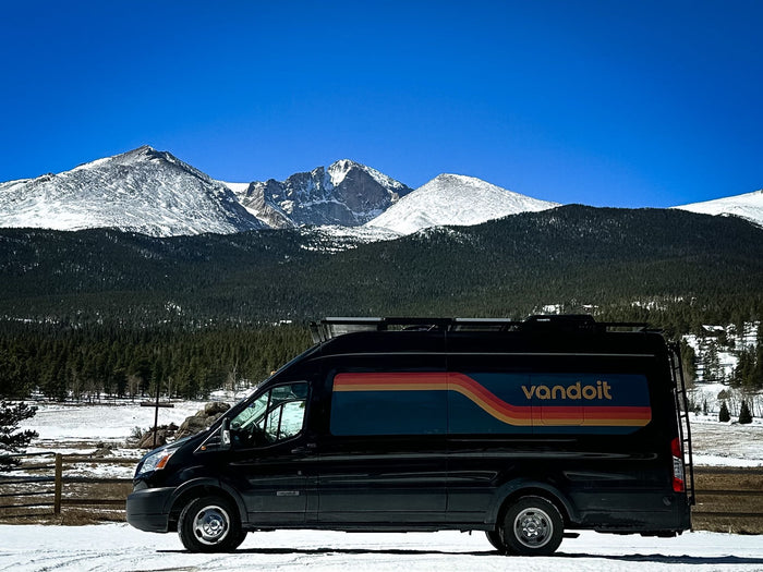 including a large arch.|An RV rental van parked among the unique Niobrara Chalk rock formations under a bright blue sky.|Black Vandoit RV rental van parked on snowy ground