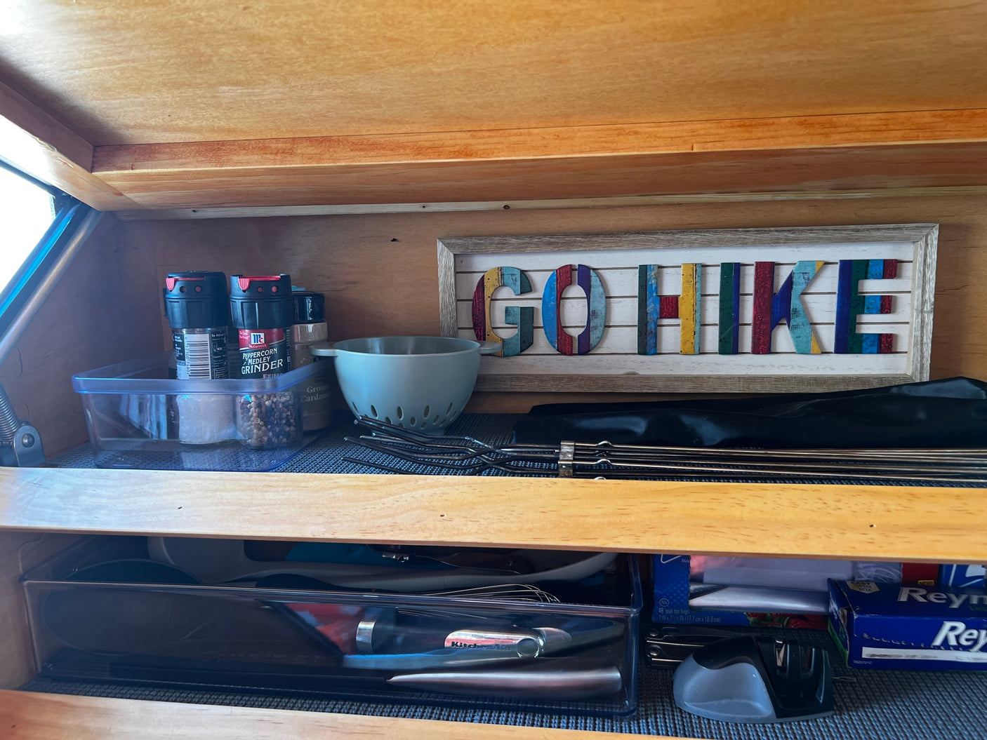 Well-organized kitchen in an RV rental, featuring McCormick spices, grilling skewers, utensils, and a "GO HIKE" sign.