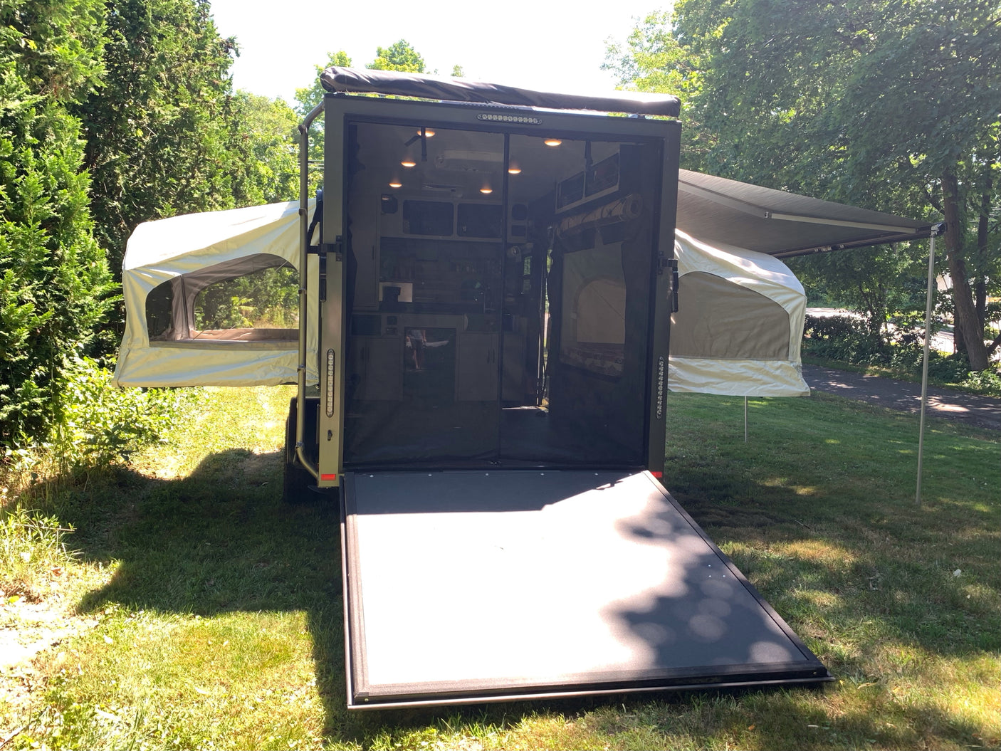 Explore nature with this unique RV rental: a converted cargo trailer featuring pop-out tents and an awning for versatile camping.