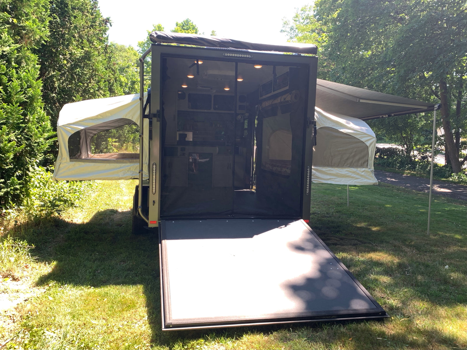 Explore nature with this unique RV rental: a converted cargo trailer featuring pop-out tents and an awning for versatile camping.