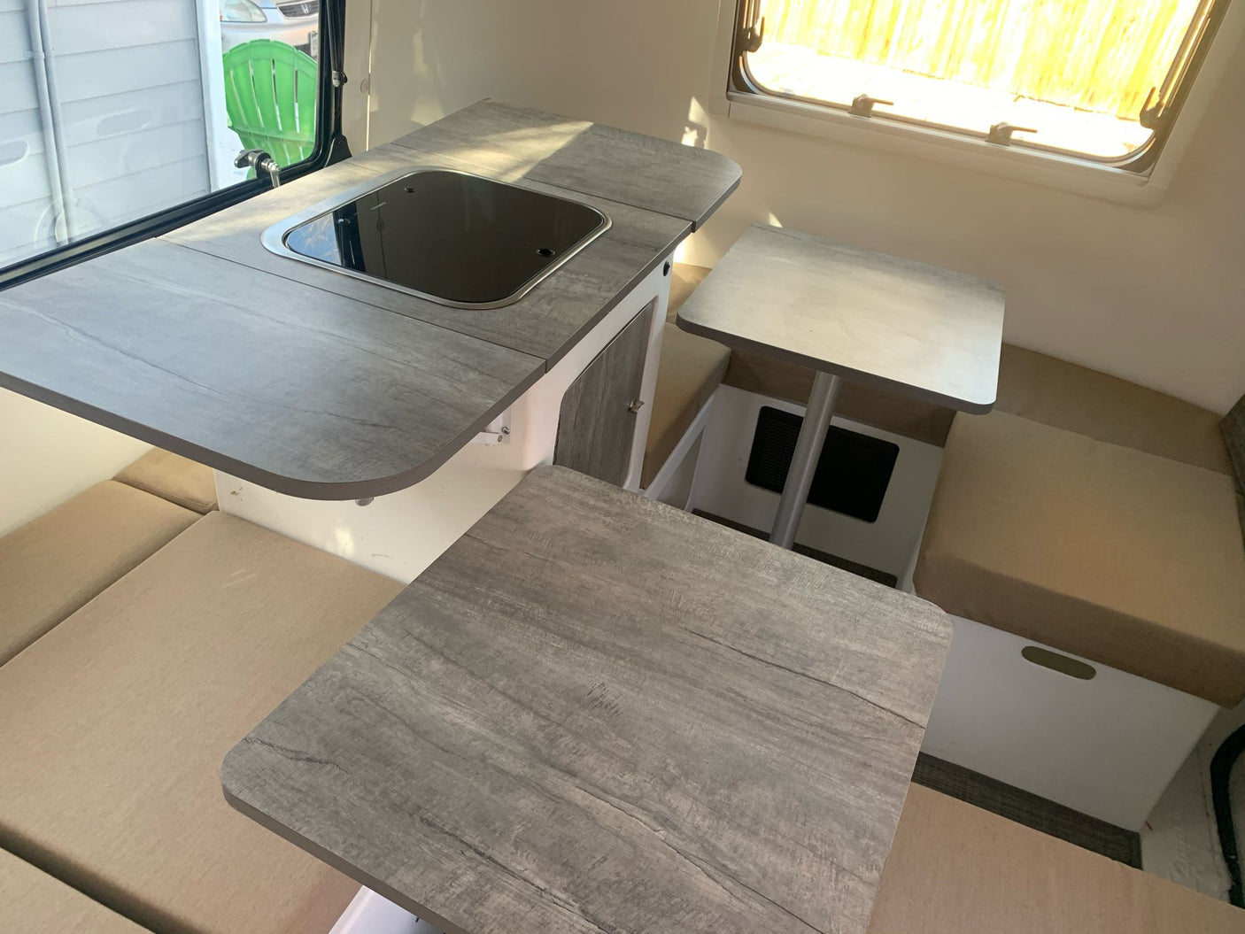 Inside this RV rental: a compact kitchen with integrated sink/cooktop, two tables, and comfortable seating for travelers.