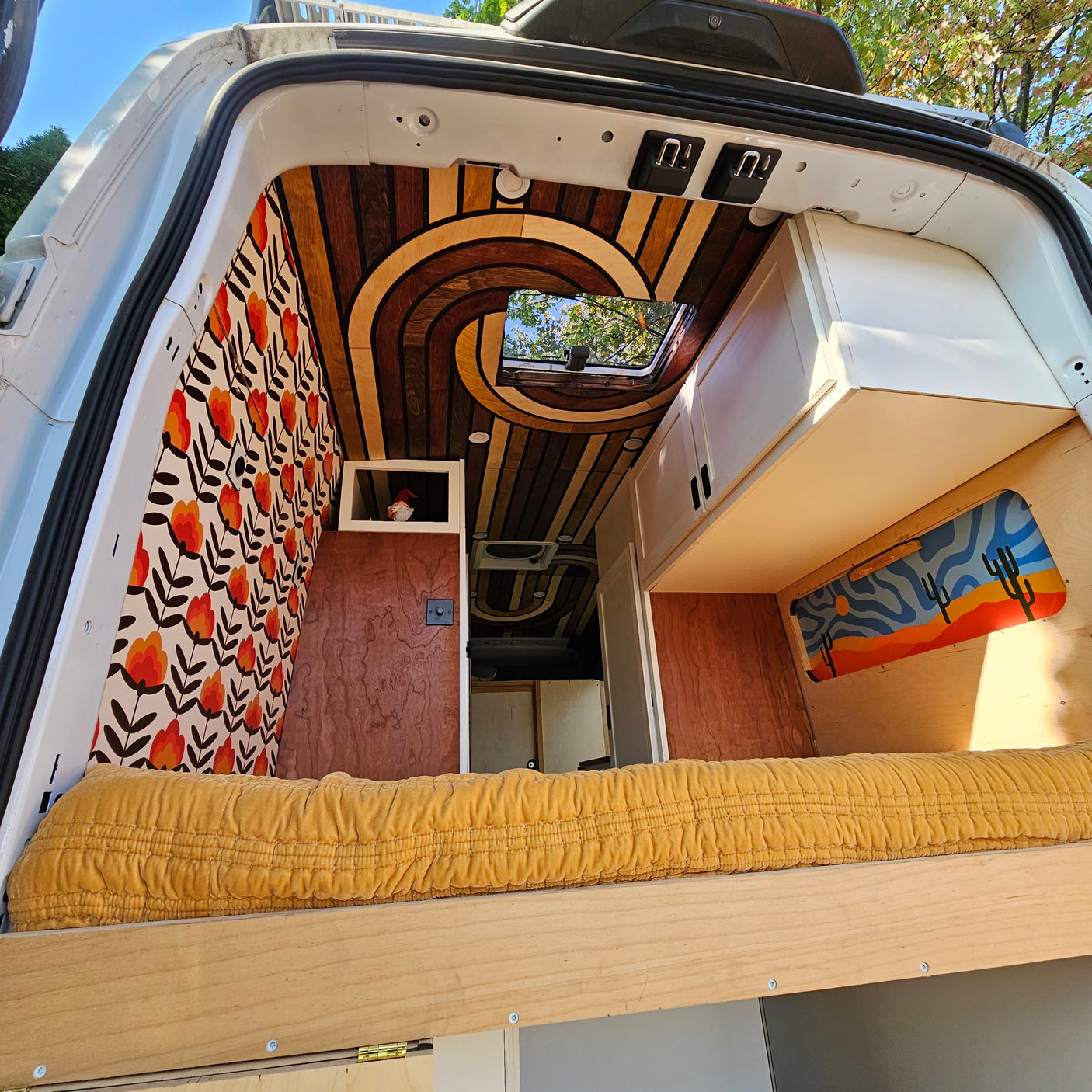 Inside a unique RV rental: custom wood swirl ceiling, floral walls, cozy bed, and desert art. Ready for adventure!