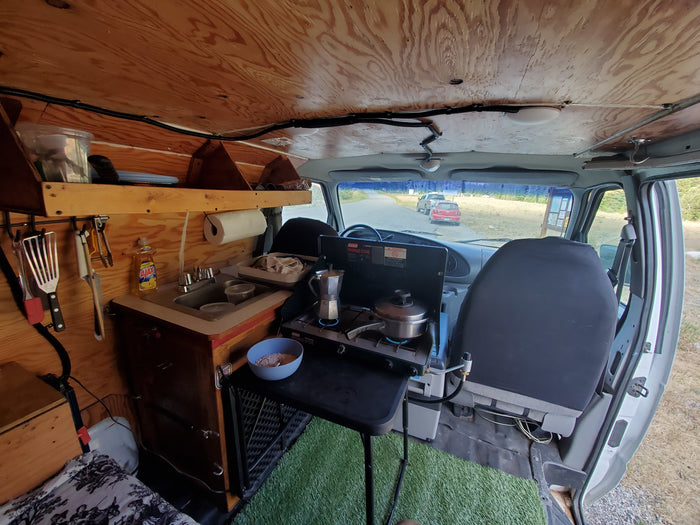 Cozy camper van interior: compact kitchen with sink, stove & wood paneling. Perfect setup for an RV rental trip.